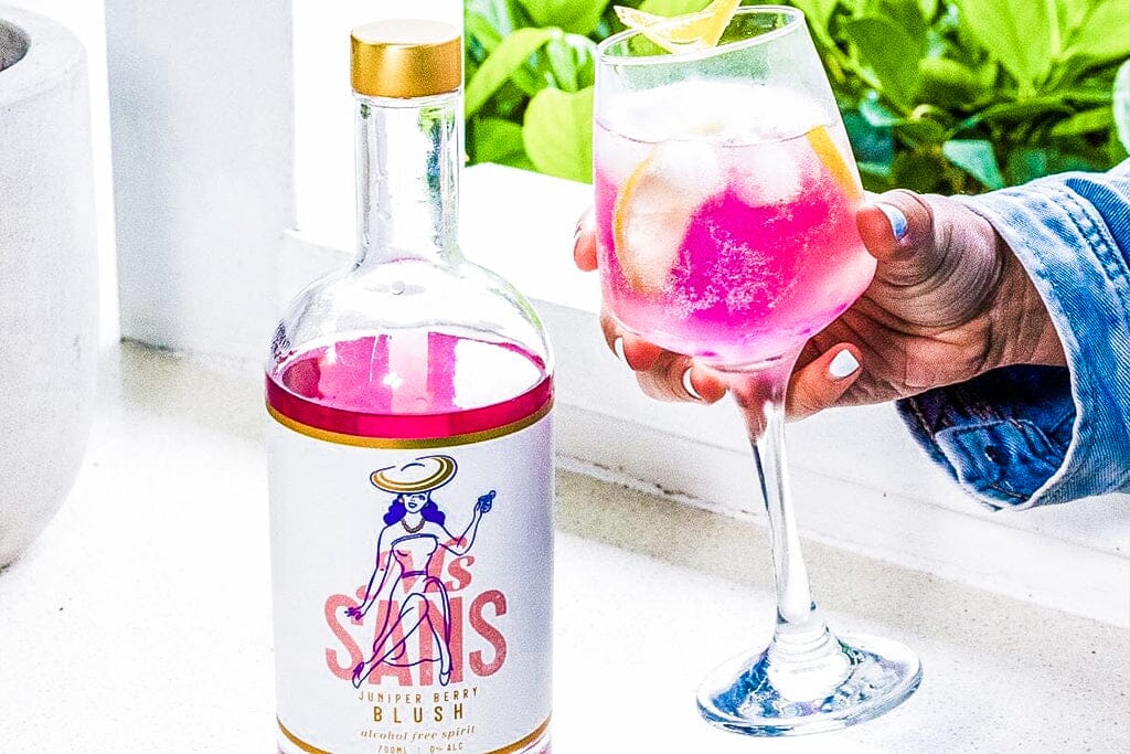 Hand holding fizzy pink gin mocktail made using qarbo sparkling water maker Sans Drinks