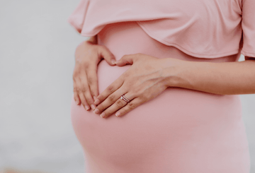 Pregnant woman holding her belly with heart hands