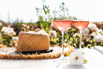 Two glasses of rose next to a hat outdoors