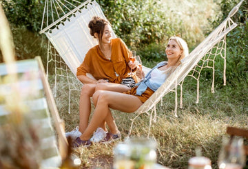 Two happy women on a hammock drinking non-alcoholic wine