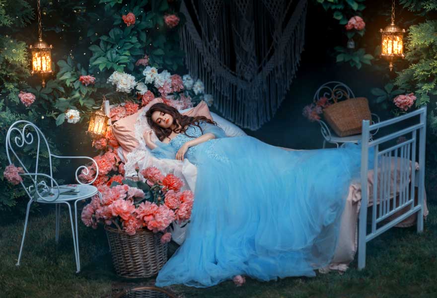 A woman wearing a blue gown sleeping in a bed surrounded by flowers