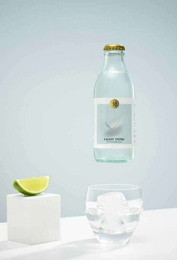 Bottle of StrangeLove Light Tonic Water above a classic gin and tonic mocktail in a glass with a single large ice cube