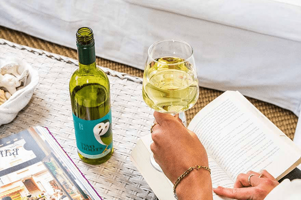 A woman reading holds a wine glass filled with Two Hoots non-alcoholic white wine Sans Drinks