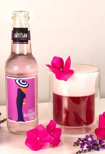 Bottle of Artisan Drinks Violet Blossom Tonic next to a glass of sour mocktail