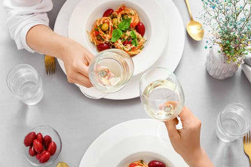 A glass of wine filled with Two Hoots Non-Alcoholic Wine and a plate with pasta Sans Drinks